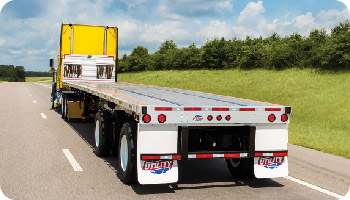 A yellow shipping container loaded onto a flatbed trailer driving down a highway, representing efficient truck rental Dubai services through green fields.