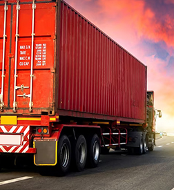 A red cargo truck is driving down a highway under a vibrant pink and orange sunset sky, conveying a sense of motion and energy.