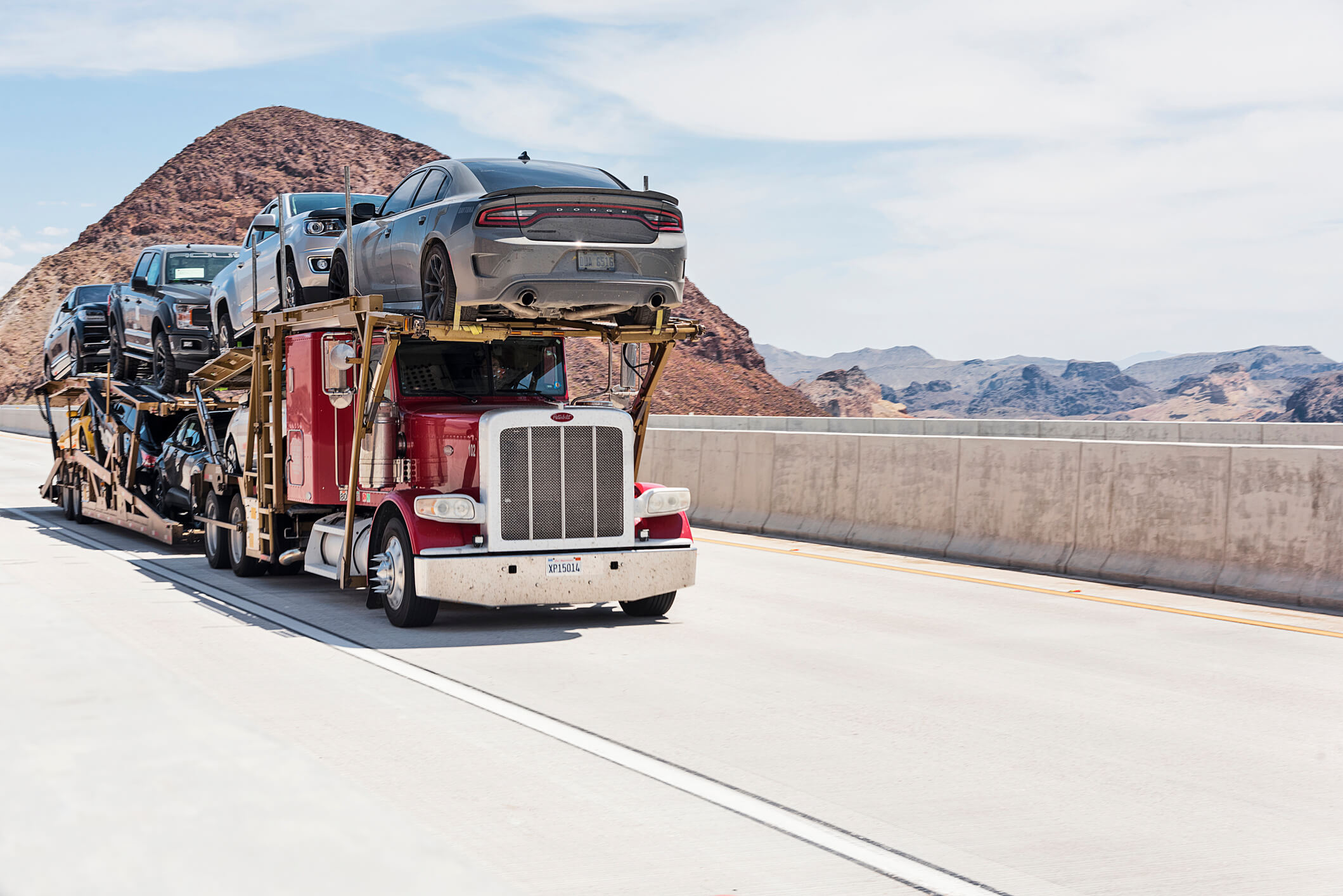 Red car transporter truck on a desert highway under blue sky, showing Drivelo’s car carrier service Dubai.