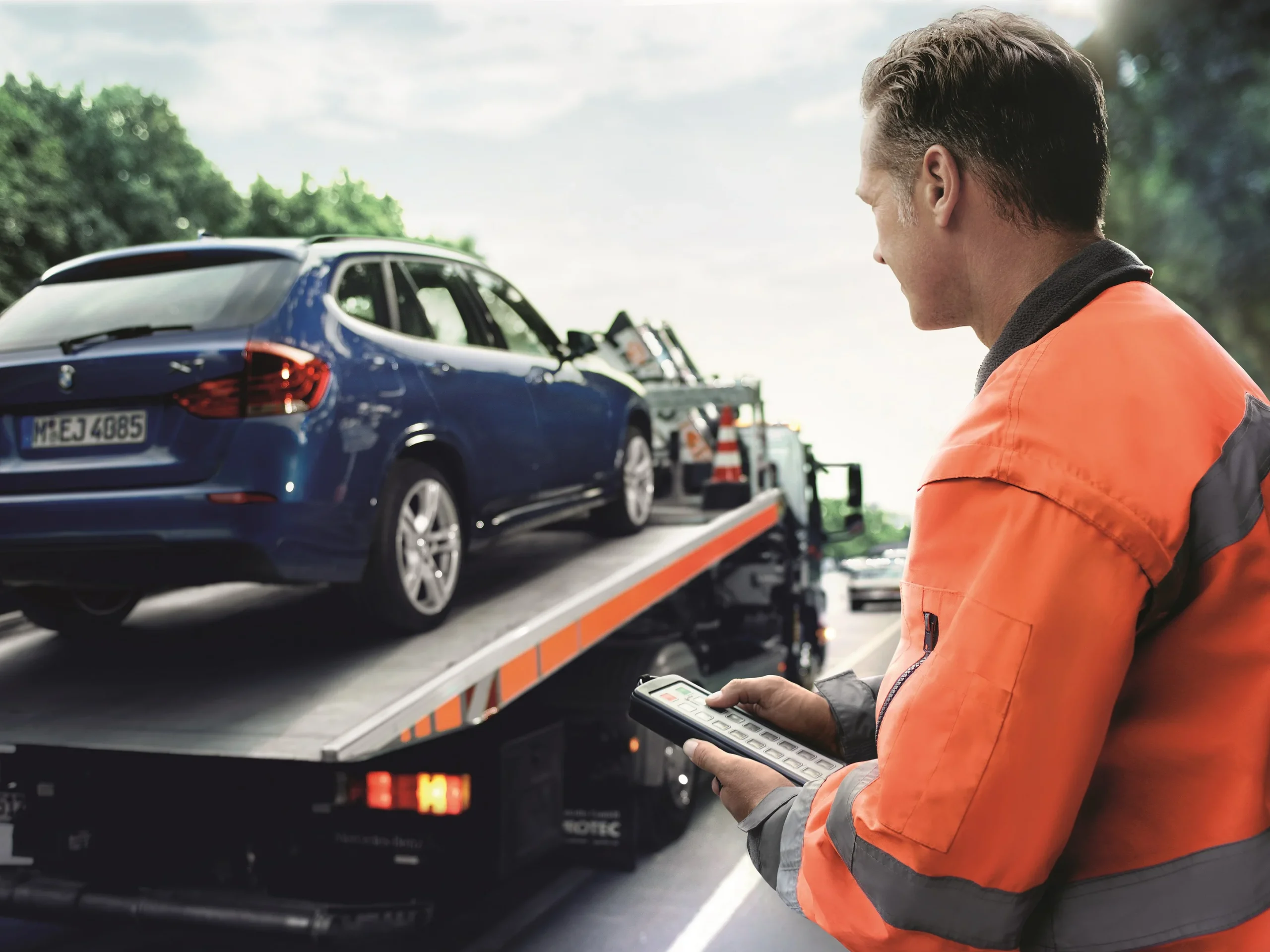 Tow truck operator beside a flatbed towing a blue car, showing Drivelo’s car carrier service Dubai.
