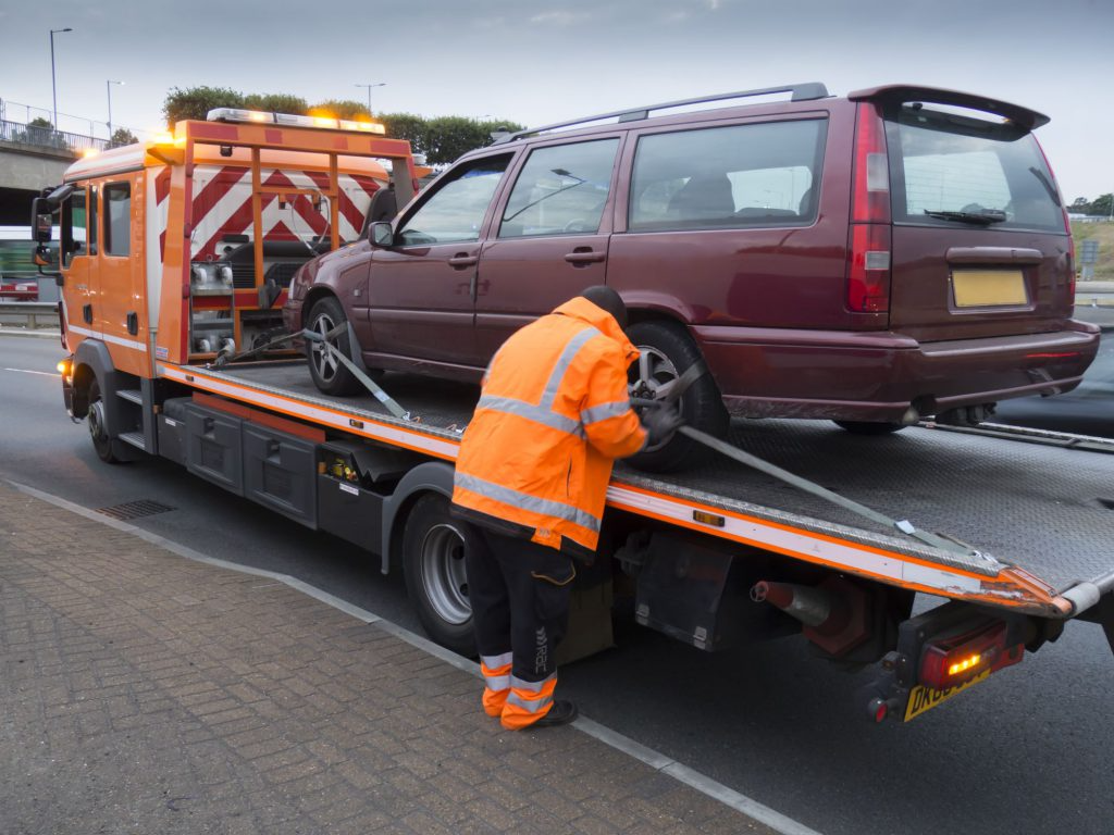 Tow truck operator securing a maroon car on a flatbed, showcasing Drivelo’s car carrier service Dubai.
