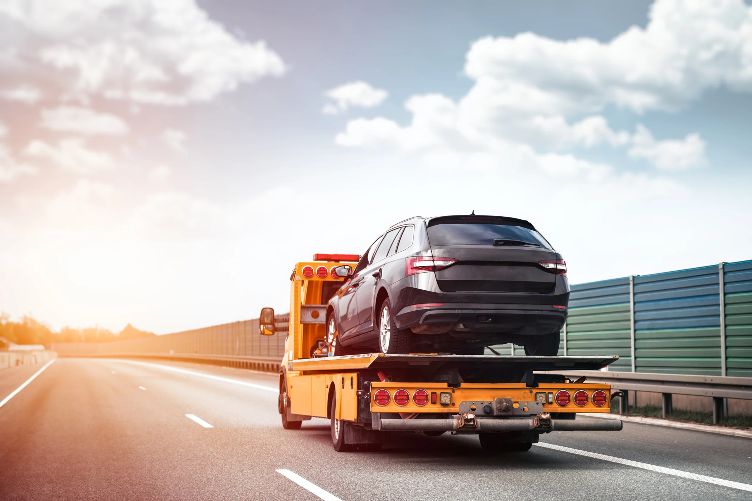 Black car on a flatbed tow truck at sunset, highlighting Drivelo’s reliable car carrier service Dubai.