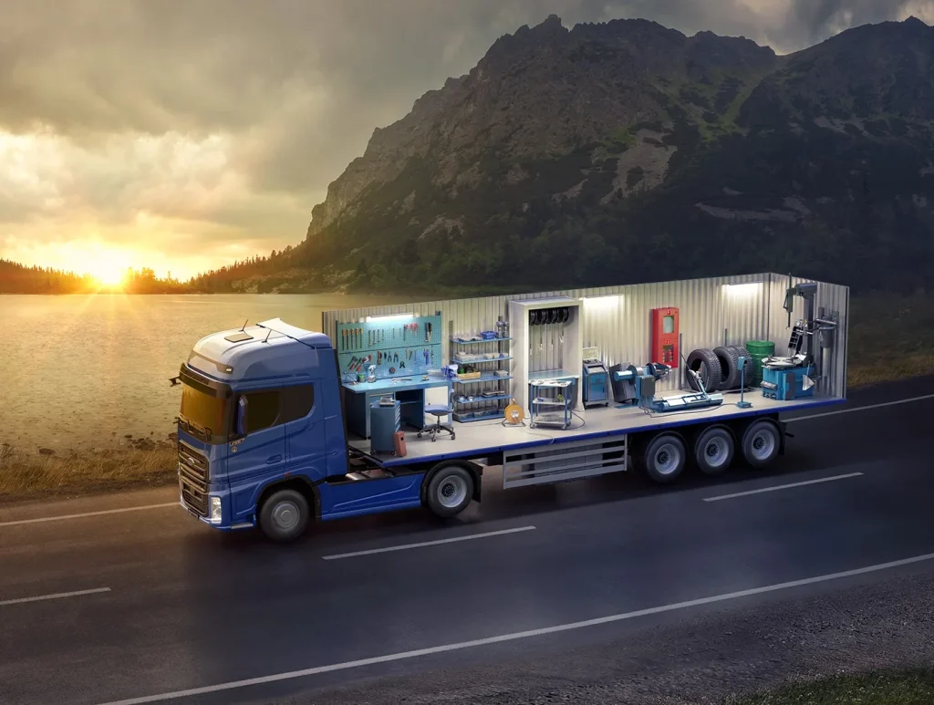 On a mountain road at sunset, a blue truck with an open side displaying a furnished living space highlights professional flatbed truck rental Dubai services.